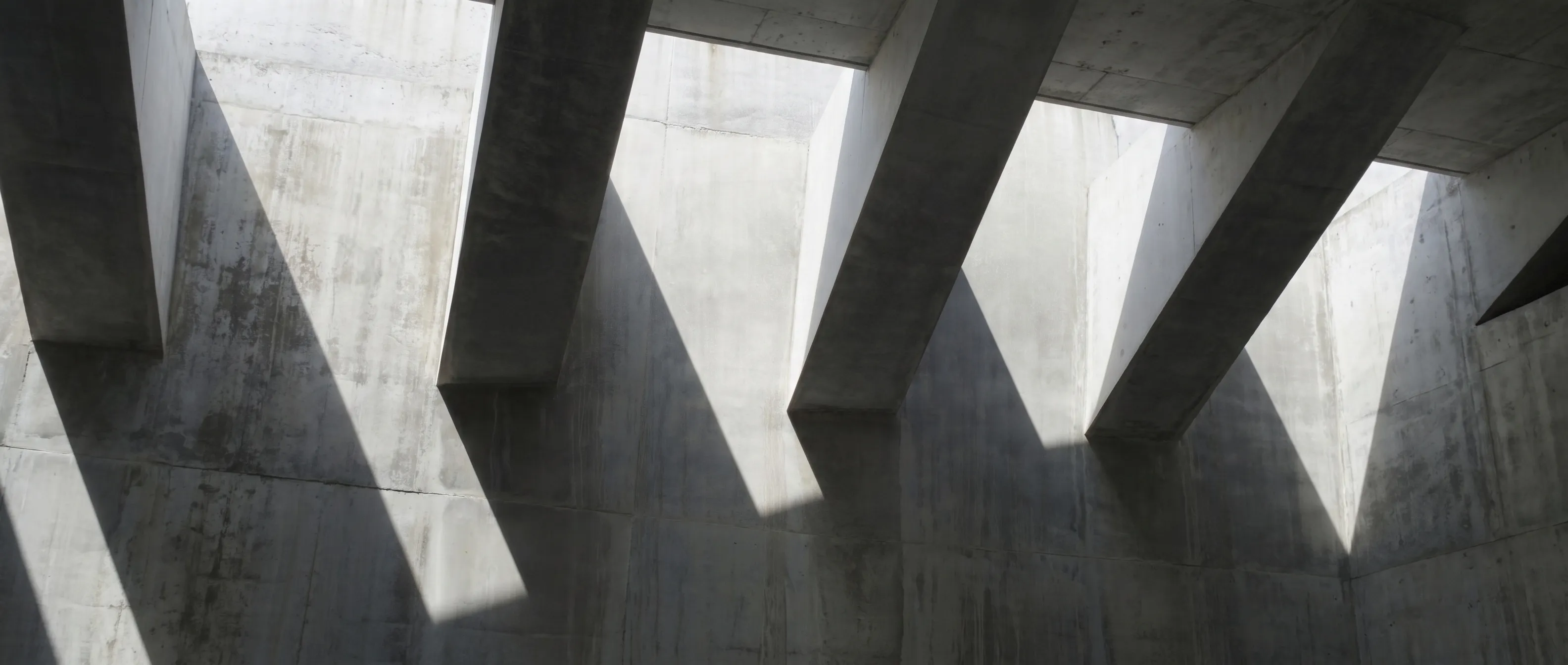Angular concrete beams with daylight falling between them, casting diagonal shadows.