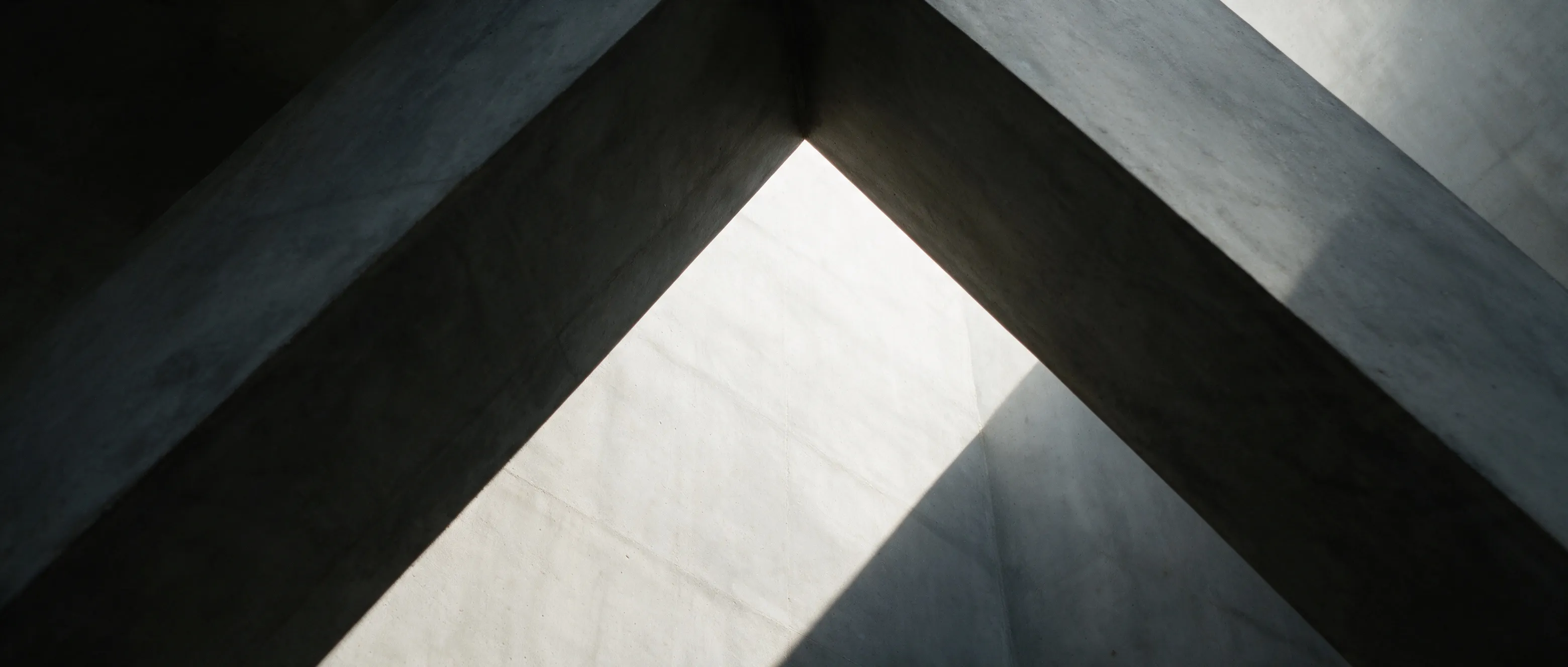 Angular concrete beams meeting overhead with daylight falling between them.